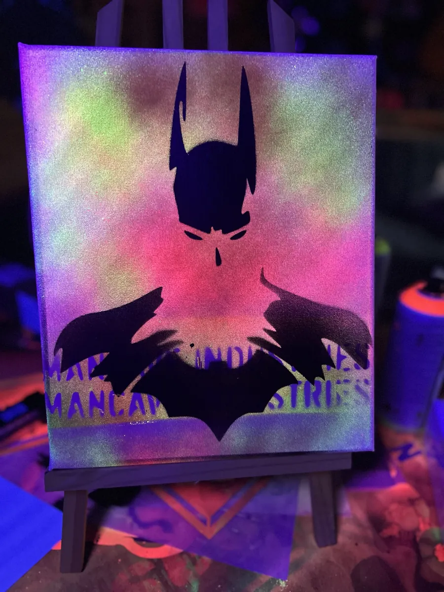 Black caped figure over a pastel spray haze, under blacklight