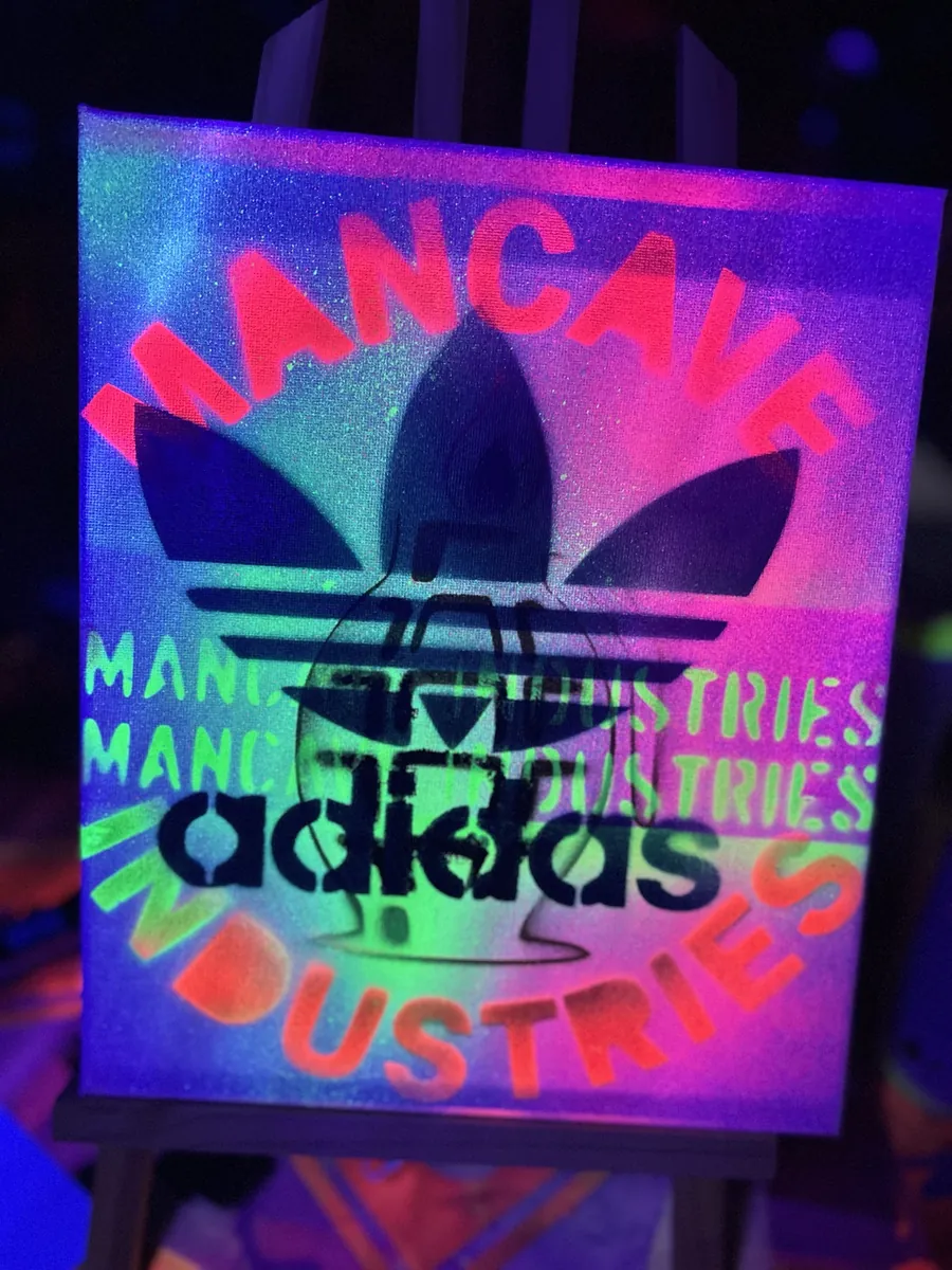 Trefoil stencil ringed with Mancave Industries lettering, under blacklight