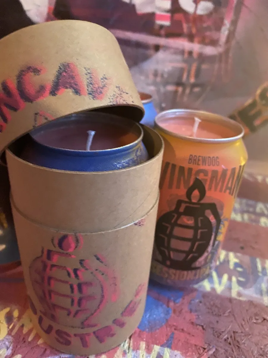 Orange can candle with black grenade stencil next to an open kraft tube