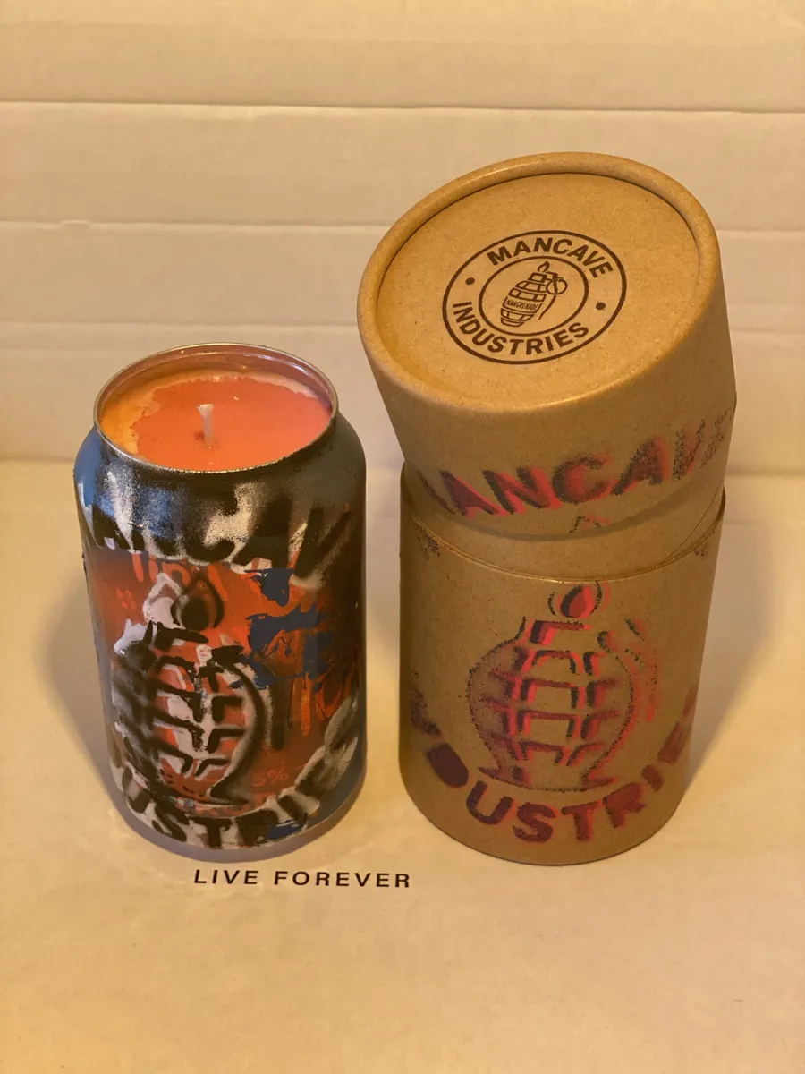 Orange and black sprayed can candle with Mancave Industries stencil, next to its kraft tube