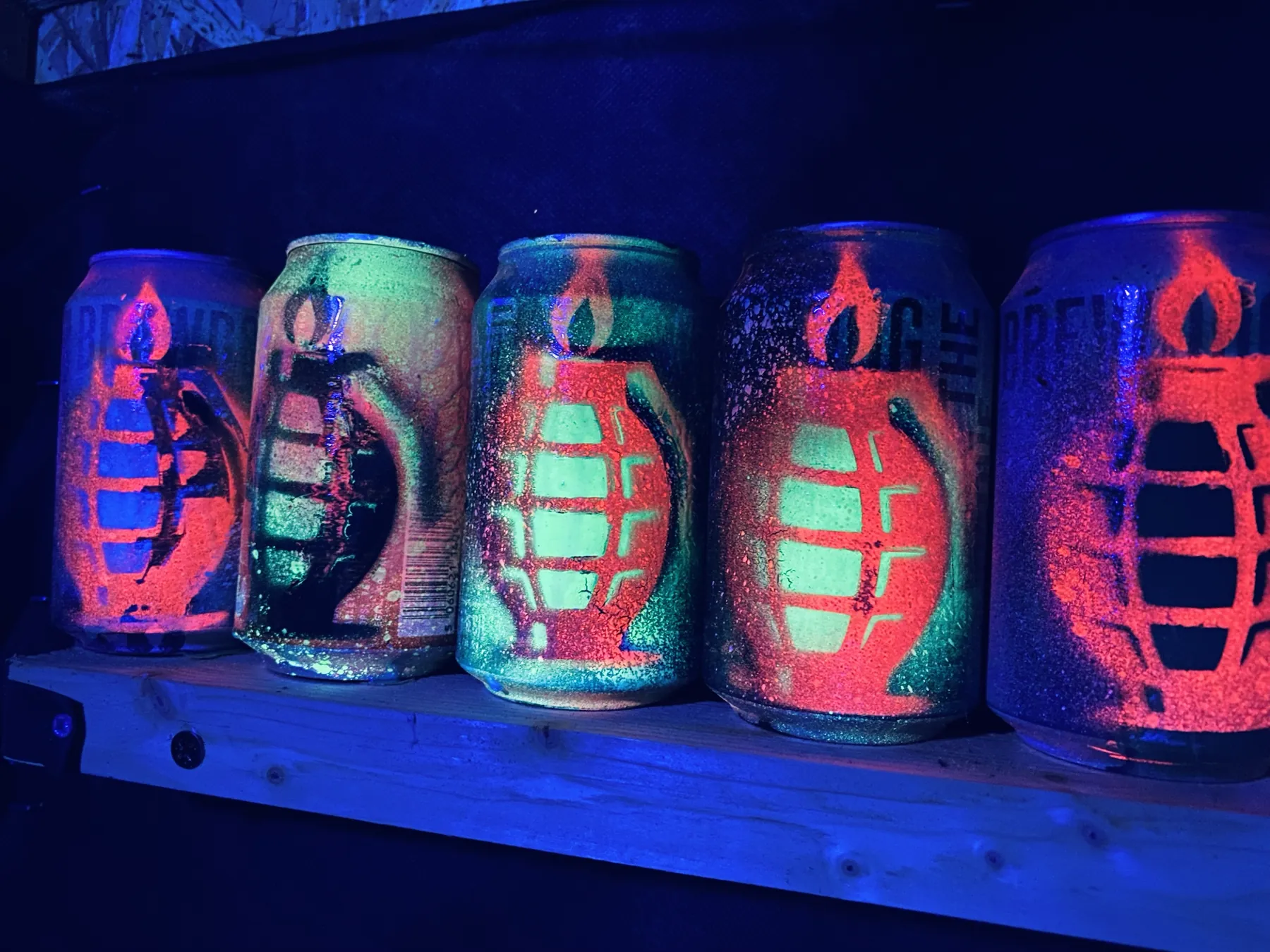 Five Mangrenades on the shed shelf, their grenade stencils glowing red and green under a blacklight