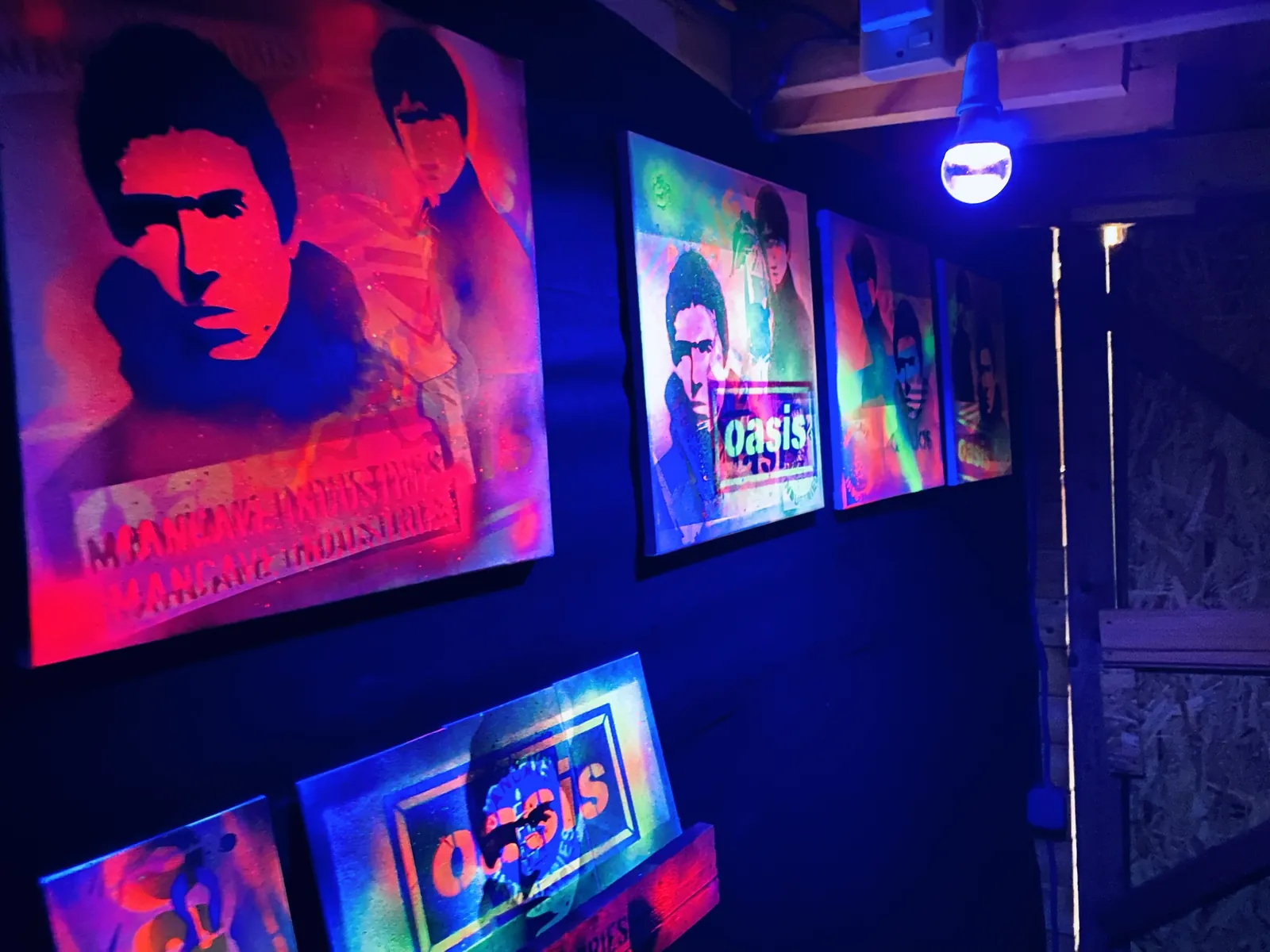 The shed wall under blacklight, hung with stencilled canvases