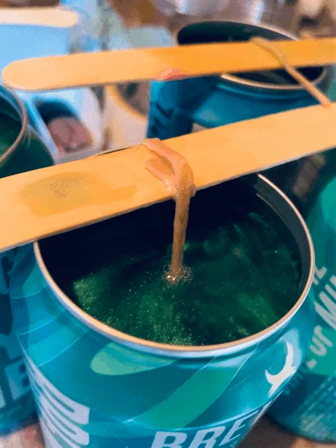 Wicks held upright on lolly sticks across freshly poured cans